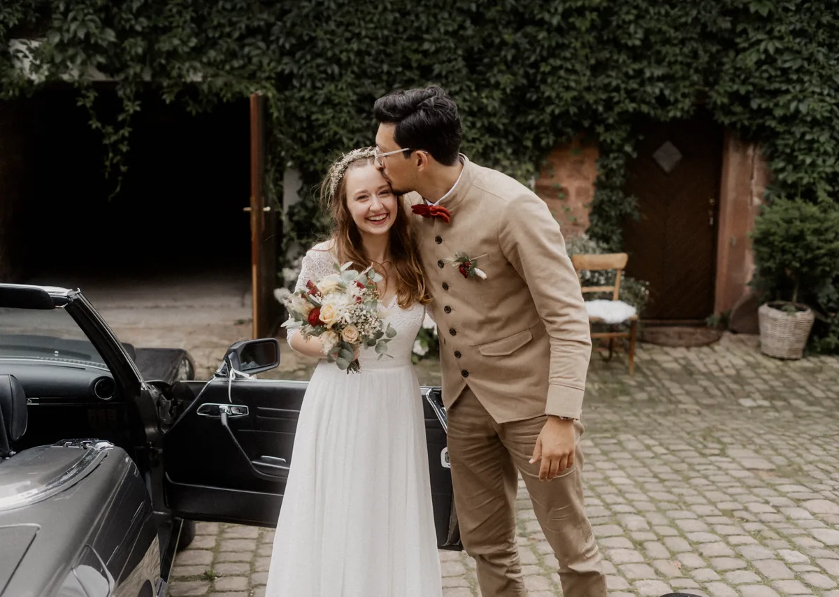 Lachendes Hochzeitspaar an einem Cabrio